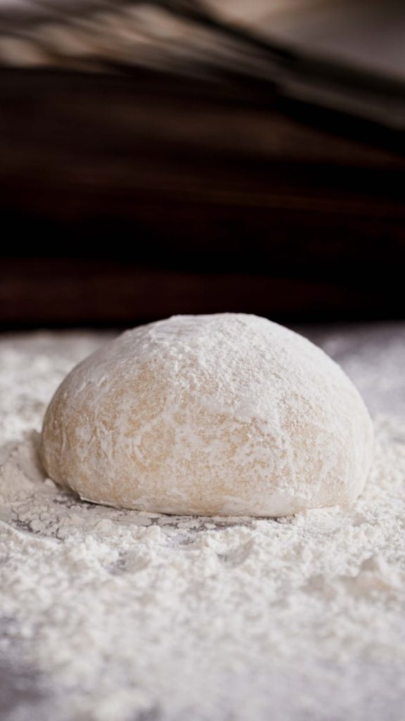 pexels-photo-20281829 A rustic dough ball dusted with flour on a wooden baking surface, ready for kneading or baking.